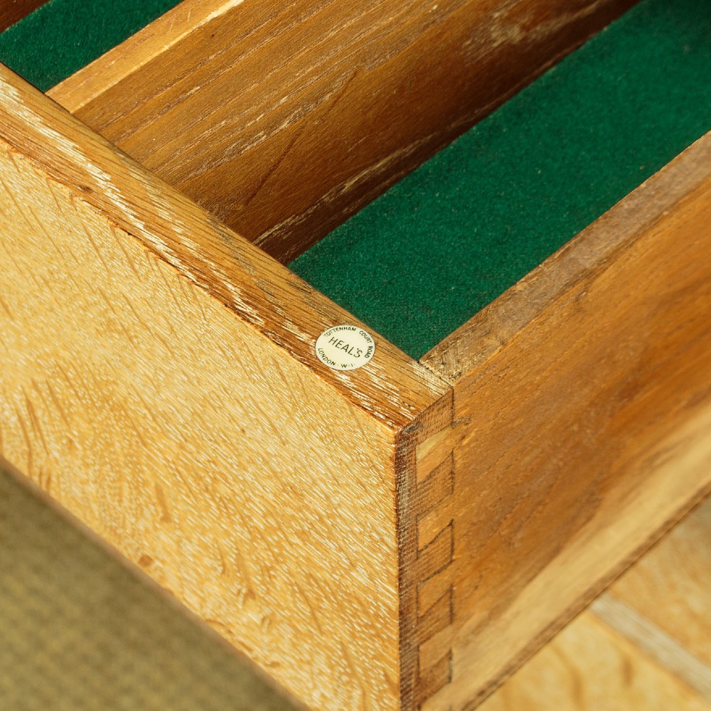 A 1920s limed oak sideboard featuring a central bank of three drawers flanked by two panelled cupboard doors on slab feet. View IX