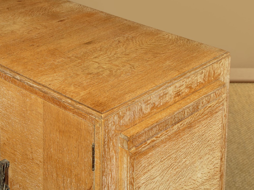 A 1920s limed oak sideboard featuring a central bank of three drawers flanked by two panelled cupboard doors on slab feet. View X