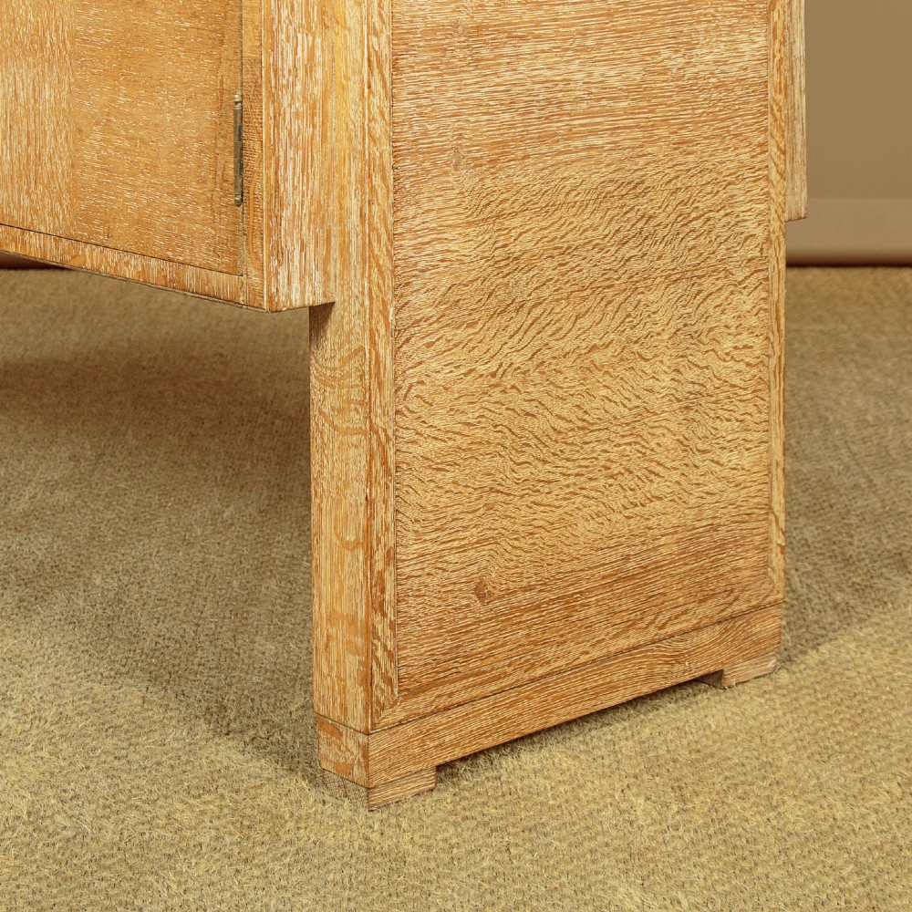 A 1920s limed oak sideboard featuring a central bank of three drawers flanked by two panelled cupboard doors on slab feet. View XIII
