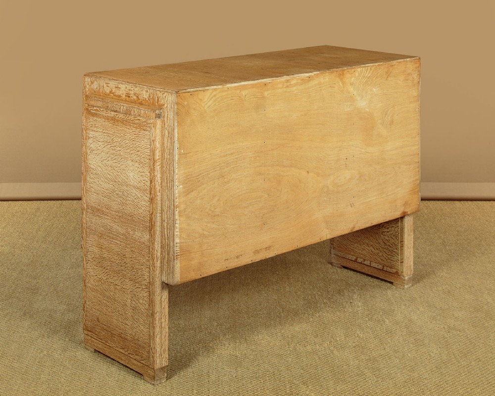 A 1920s limed oak sideboard featuring a central bank of three drawers flanked by two panelled cupboard doors on slab feet. View XIV