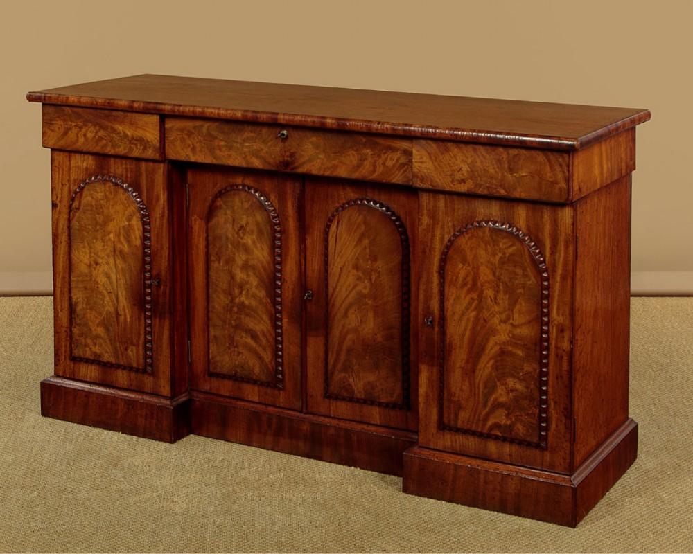A William IV mahogany four-door breakfront sideboard featuring flame mahogany drawer fronts and arched cupboard doors set on a solid plinth base.