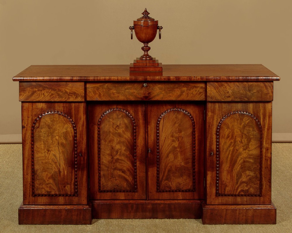 A William IV mahogany four-door breakfront sideboard featuring flame mahogany drawer fronts and arched cupboard doors set on a solid plinth base. View II