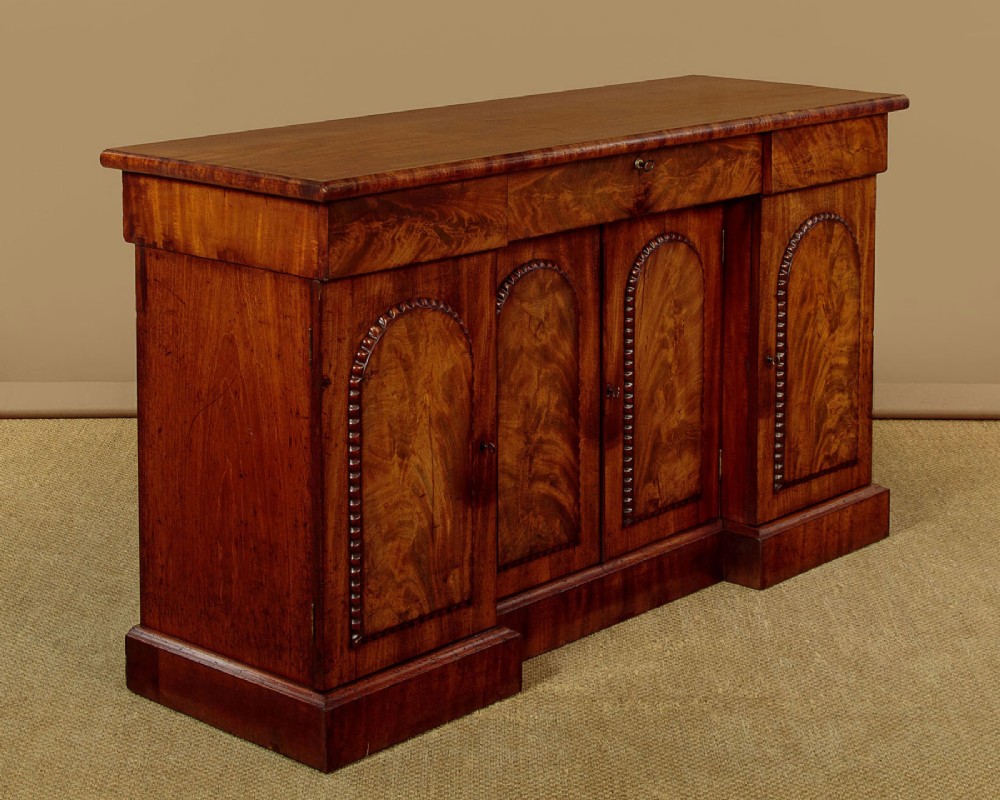 A William IV mahogany four-door breakfront sideboard featuring flame mahogany drawer fronts and arched cupboard doors set on a solid plinth base. View III