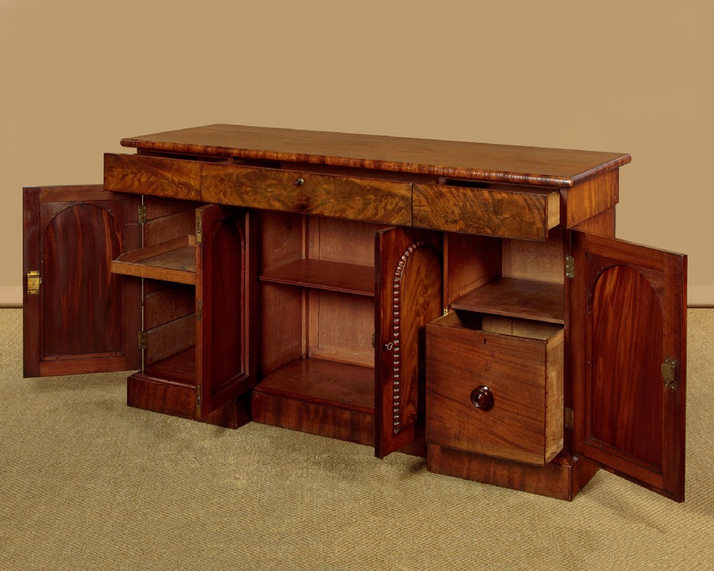 A William IV mahogany four-door breakfront sideboard featuring flame mahogany drawer fronts and arched cupboard doors set on a solid plinth base. View IV