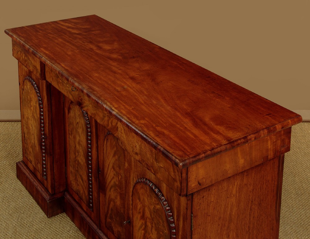 A William IV mahogany four-door breakfront sideboard featuring flame mahogany drawer fronts and arched cupboard doors set on a solid plinth base. View V