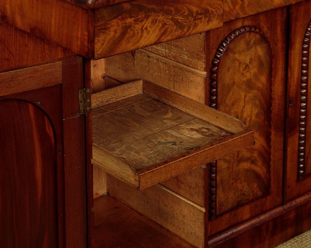 A William IV mahogany four-door breakfront sideboard featuring flame mahogany drawer fronts and arched cupboard doors set on a solid plinth base. View IX