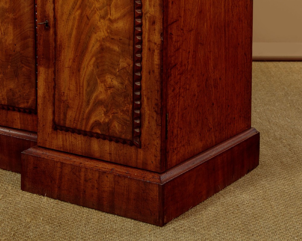 A William IV mahogany four-door breakfront sideboard featuring flame mahogany drawer fronts and arched cupboard doors set on a solid plinth base. View XII