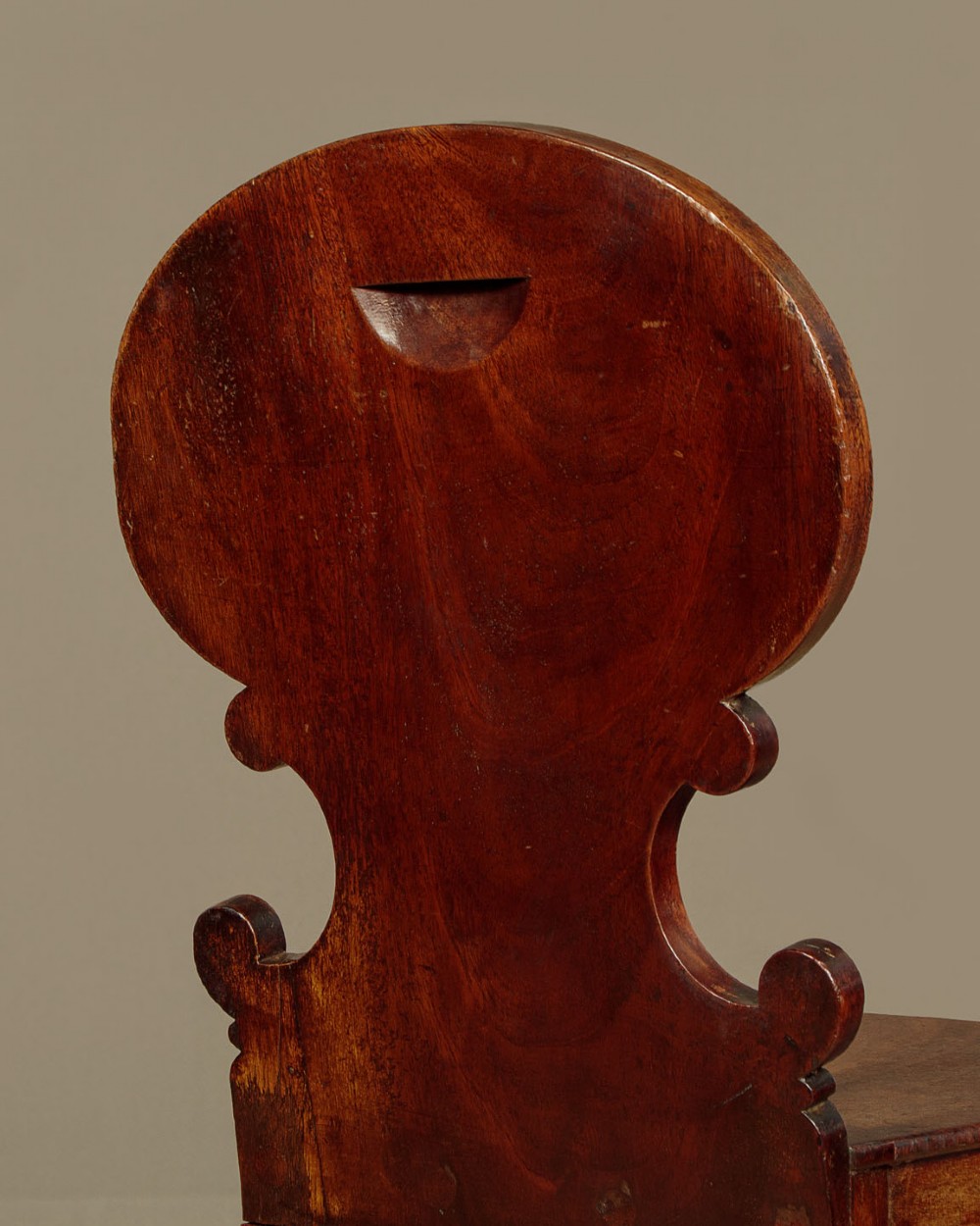 A pair of early nineteenth-century Regency mahogany hall chairs with carved oval backrests, scroll waist accents, solid wooden seats, and turned front legs. View VII