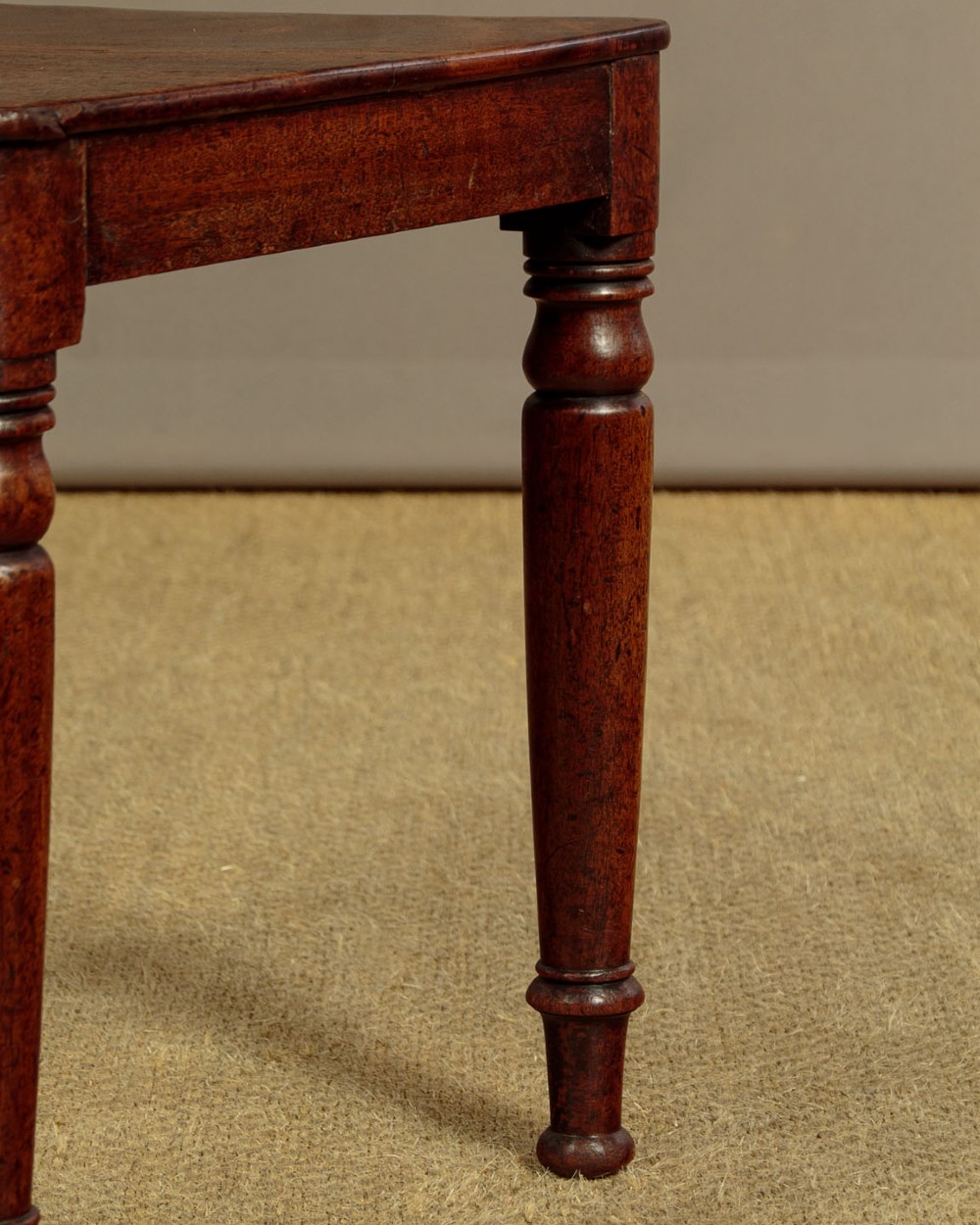 A pair of early nineteenth-century Regency mahogany hall chairs with carved oval backrests, scroll waist accents, solid wooden seats, and turned front legs. View IX