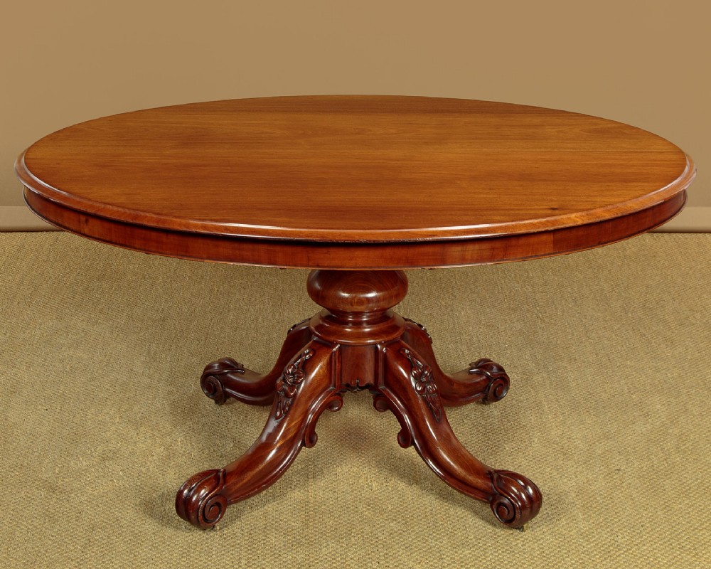 An oval mahogany pedestal dining table featuring a carved quadruped base with scroll feet.