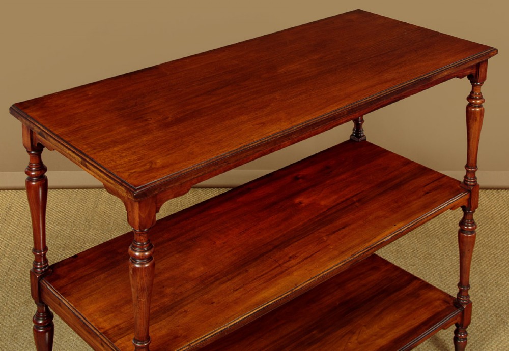 A three-tiered Victorian walnut dumb waiter featuring turned upright supports, open rectangular shelves, and brass castors. View IV