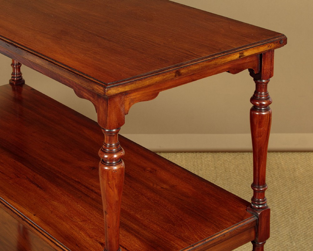 A three-tiered Victorian walnut dumb waiter featuring turned upright supports, open rectangular shelves, and brass castors. View V
