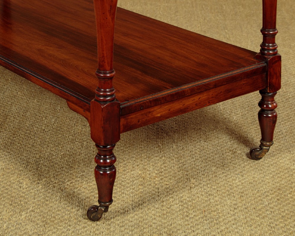 A three-tiered Victorian walnut dumb waiter featuring turned upright supports, open rectangular shelves, and brass castors. View VII