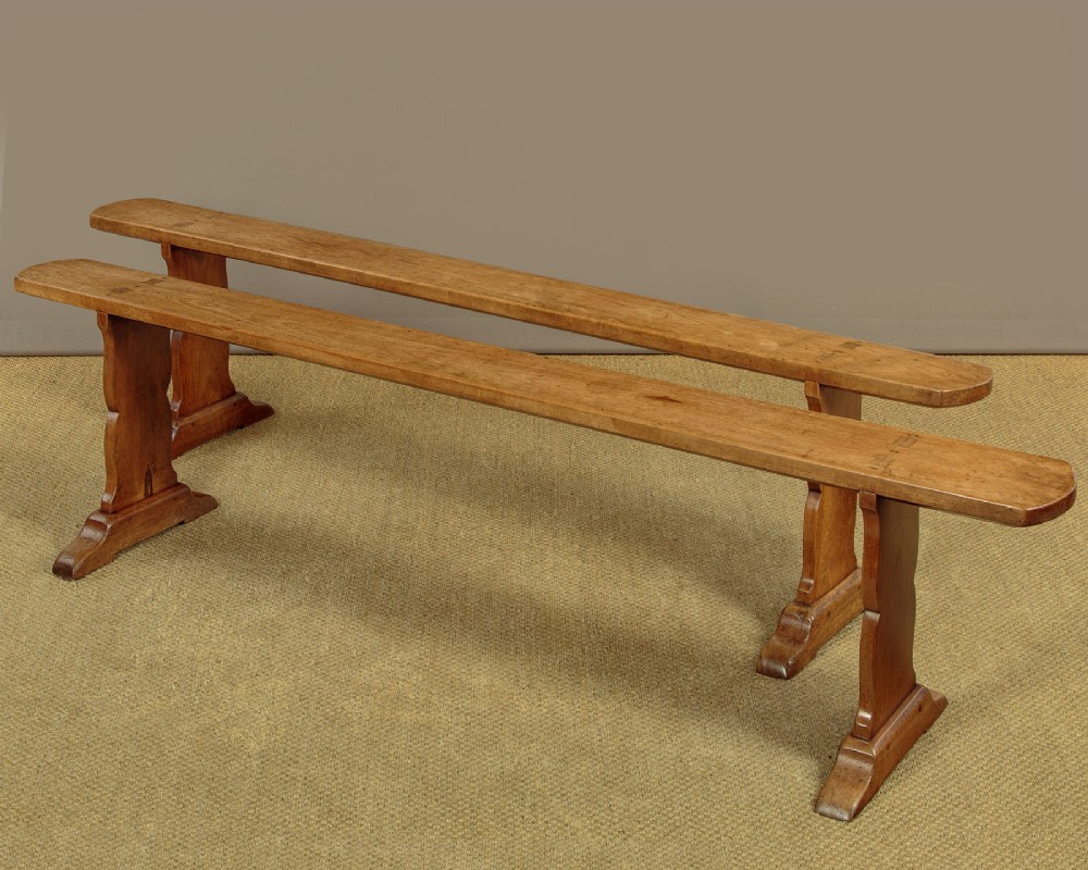 A pair of long antique French cherrywood benches featuring simple plank seats supported by shaped trestle legs. View II