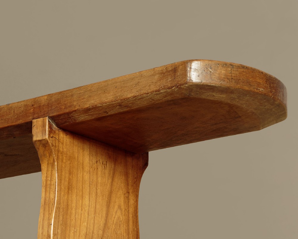 A pair of long antique French cherrywood benches featuring simple plank seats supported by shaped trestle legs. View VI