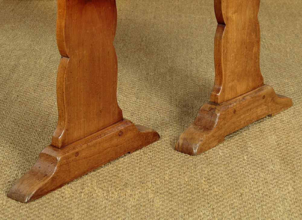 A pair of long antique French cherrywood benches featuring simple plank seats supported by shaped trestle legs. View VII