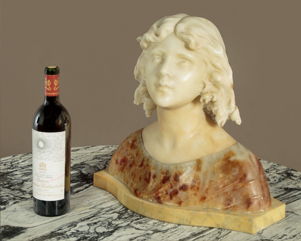 A carved alabaster bust depicting a young woman with shoulder-length wavy hair, wearing a dark amber stone dress on a matching plinth base. View II