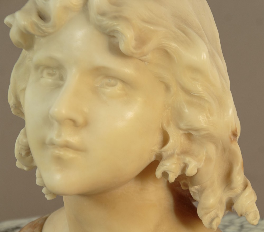 A carved alabaster bust depicting a young woman with shoulder-length wavy hair, wearing a dark amber stone dress on a matching plinth base. View VII