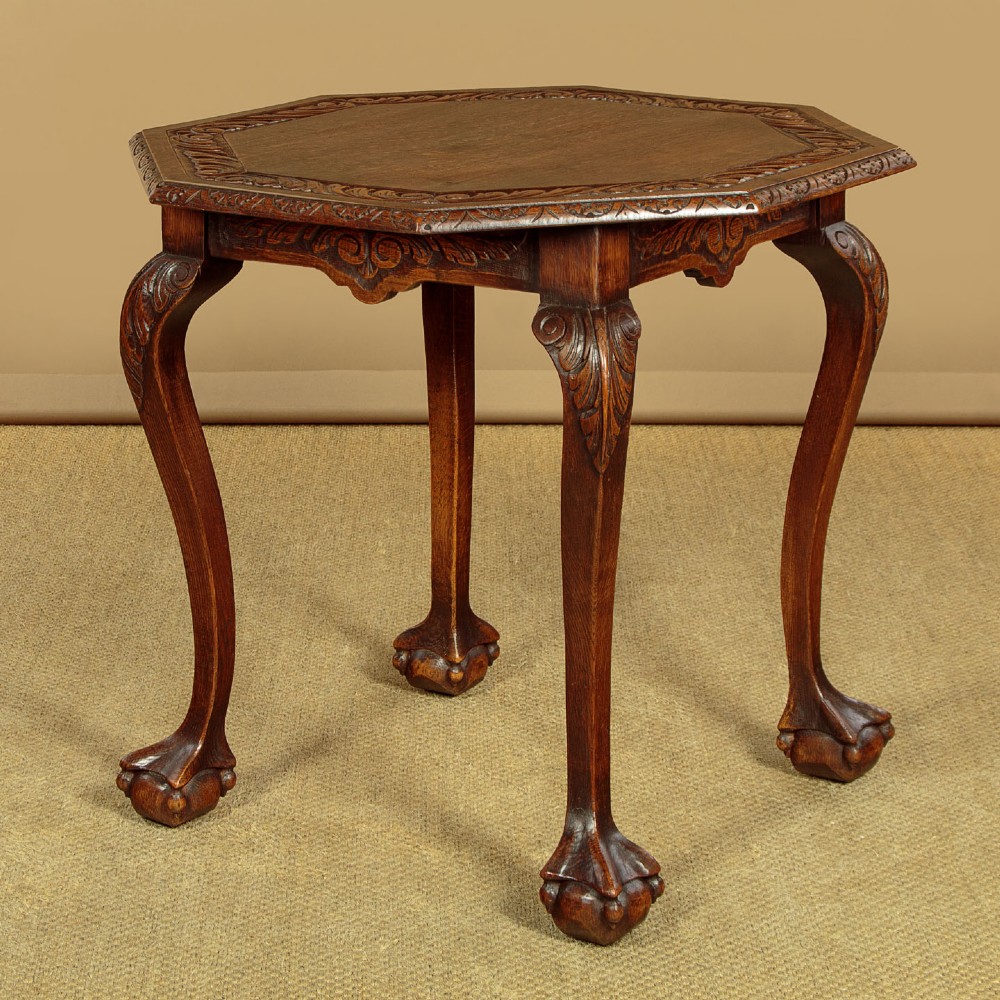 An octagonal dark carved oak side table featuring cabriole legs and carved ball and claw feet.
