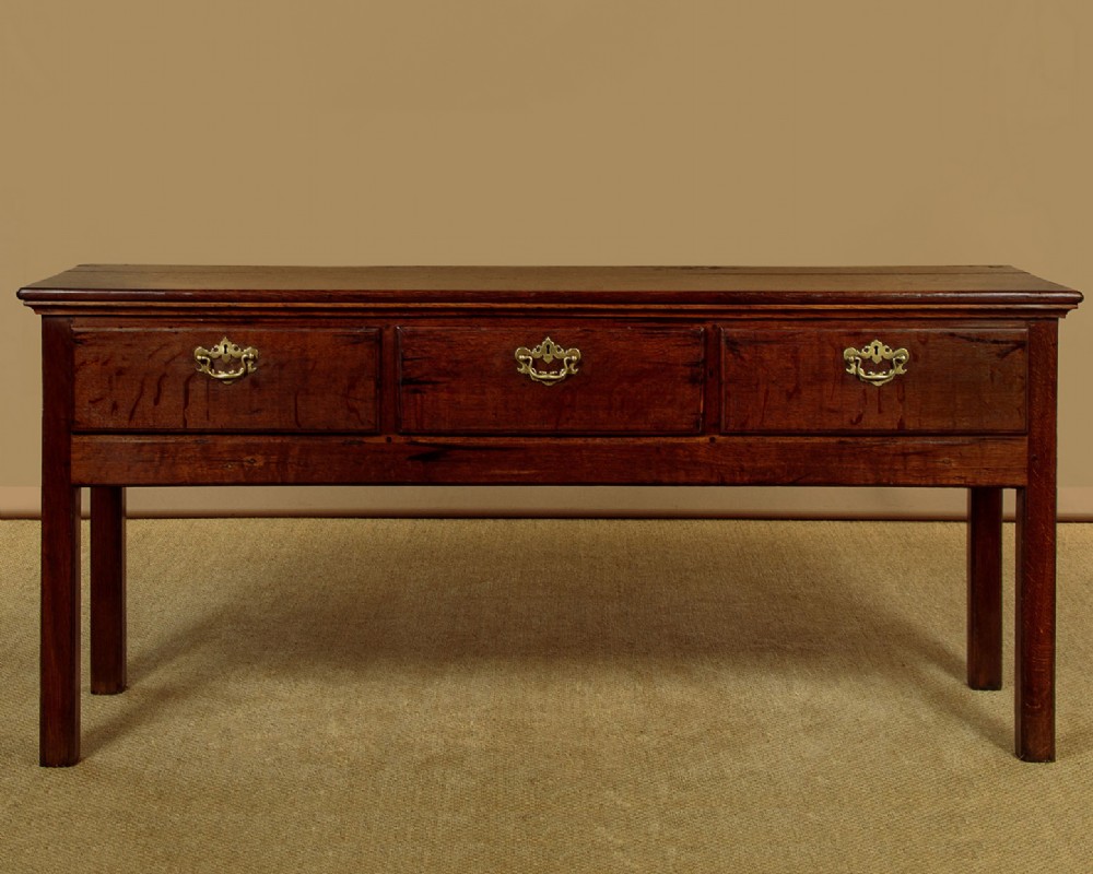 A Georgian dark oak dresser base featuring three drawers with brass handles, set on straight legs.