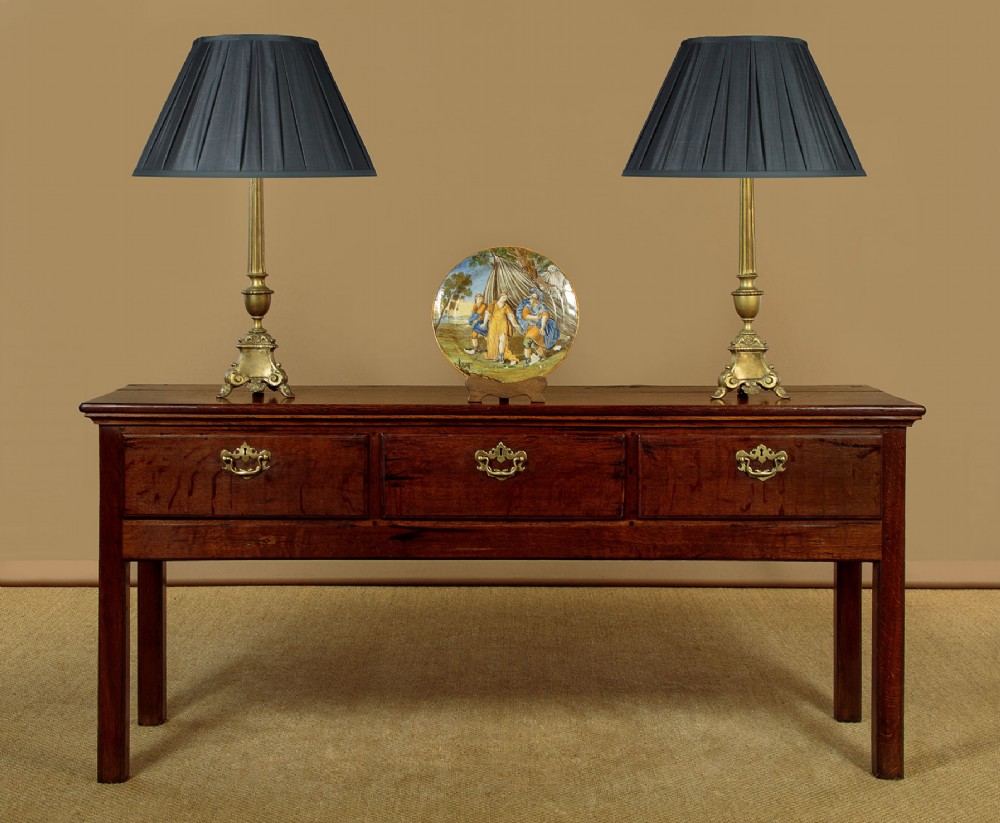 A Georgian dark oak dresser base featuring three drawers with brass handles, set on straight legs. View II