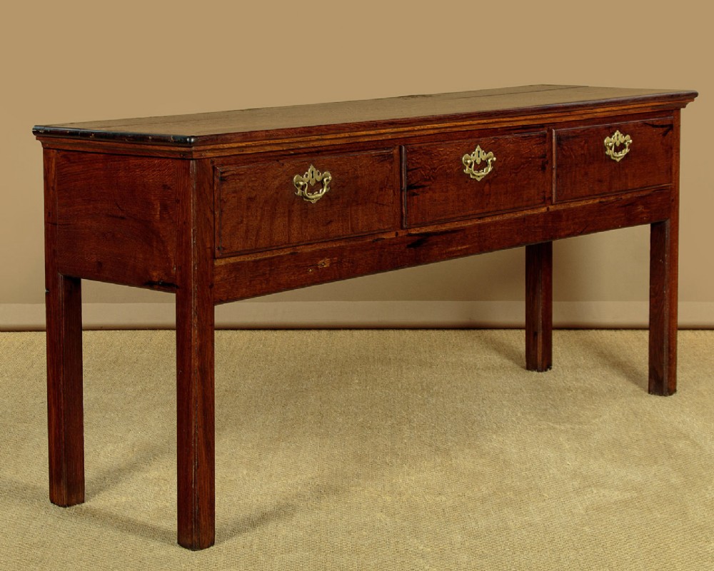 A Georgian dark oak dresser base featuring three drawers with brass handles, set on straight legs. View III