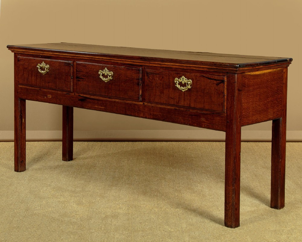 A Georgian dark oak dresser base featuring three drawers with brass handles, set on straight legs. View IV