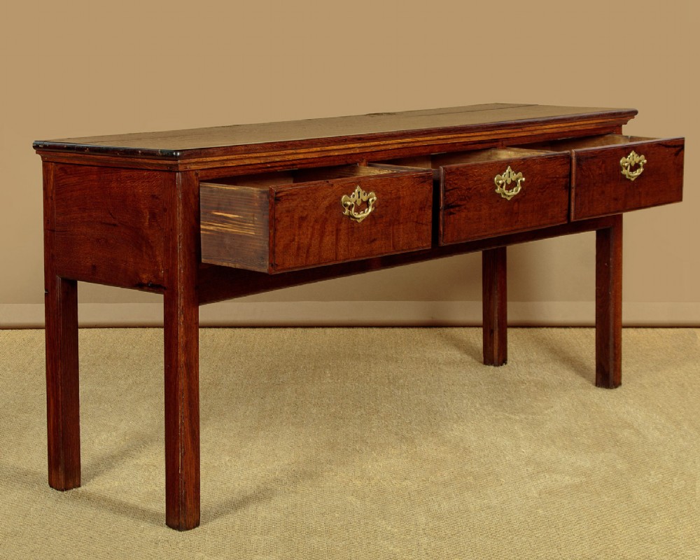 A Georgian dark oak dresser base featuring three drawers with brass handles, set on straight legs. View V