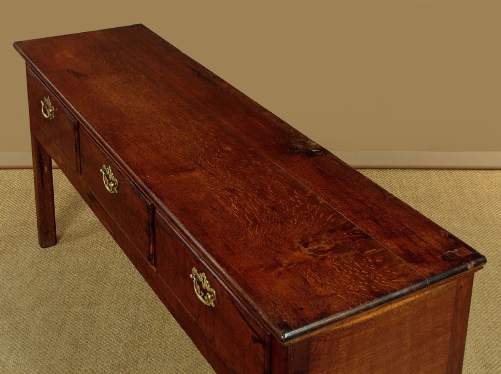 A Georgian dark oak dresser base featuring three drawers with brass handles, set on straight legs. View VI