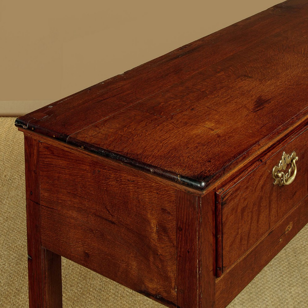 A Georgian dark oak dresser base featuring three drawers with brass handles, set on straight legs. View VII