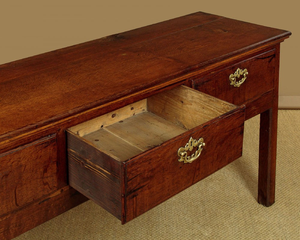 A Georgian dark oak dresser base featuring three drawers with brass handles, set on straight legs. View IX