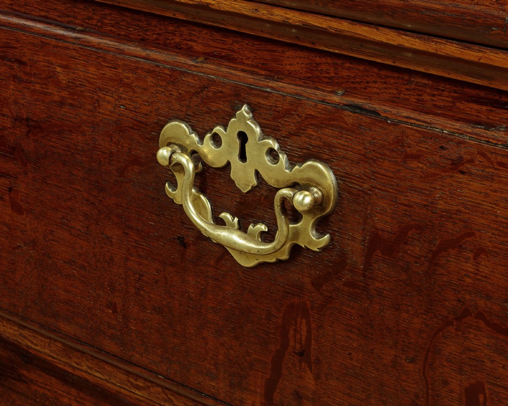 A Georgian dark oak dresser base featuring three drawers with brass handles, set on straight legs. View X