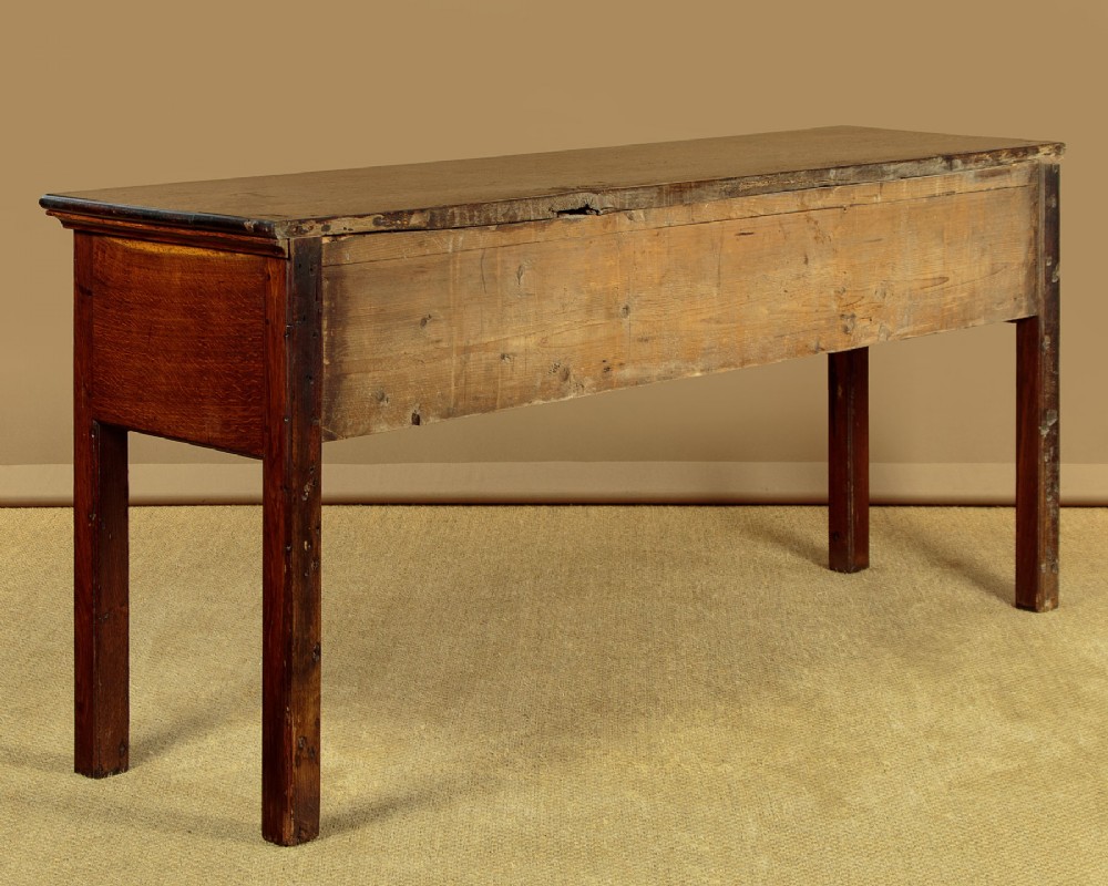 A Georgian dark oak dresser base featuring three drawers with brass handles, set on straight legs. View XII