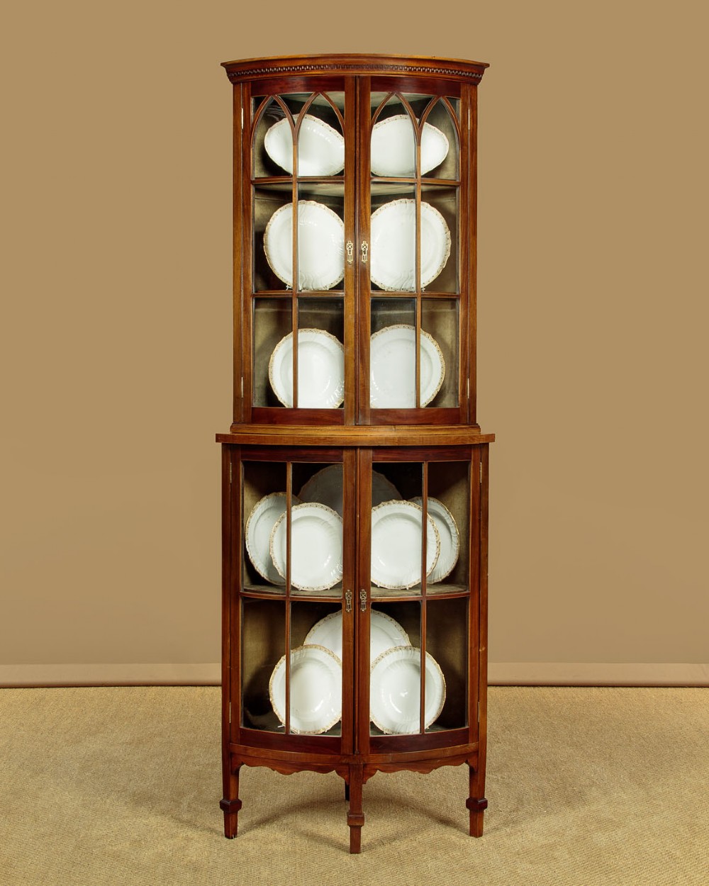 A two-tiered mahogany bow front corner display cabinet featuring upper gothic arch astragal glazing and lower glass panels. View II