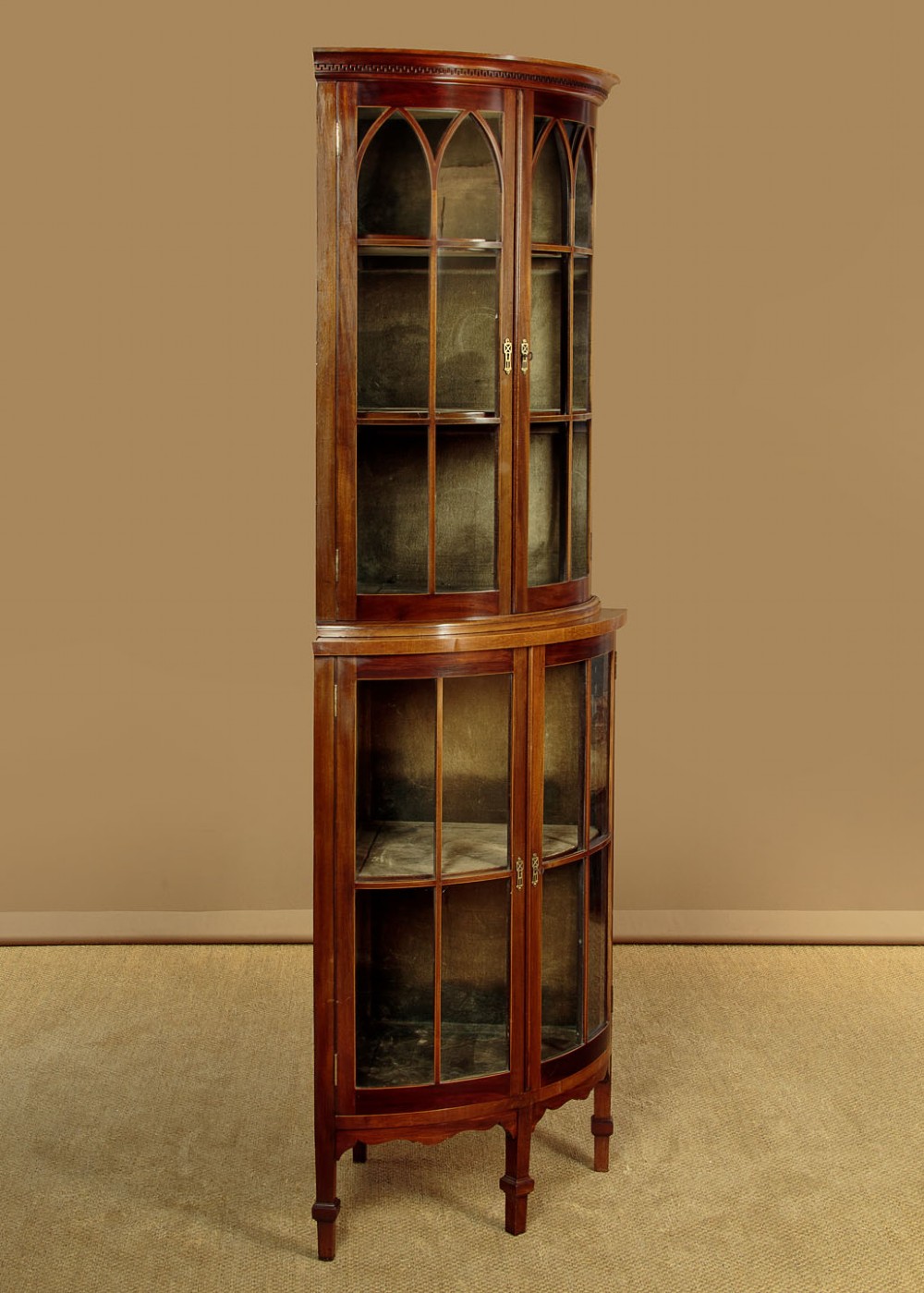 A two-tiered mahogany bow front corner display cabinet featuring upper gothic arch astragal glazing and lower glass panels. View III
