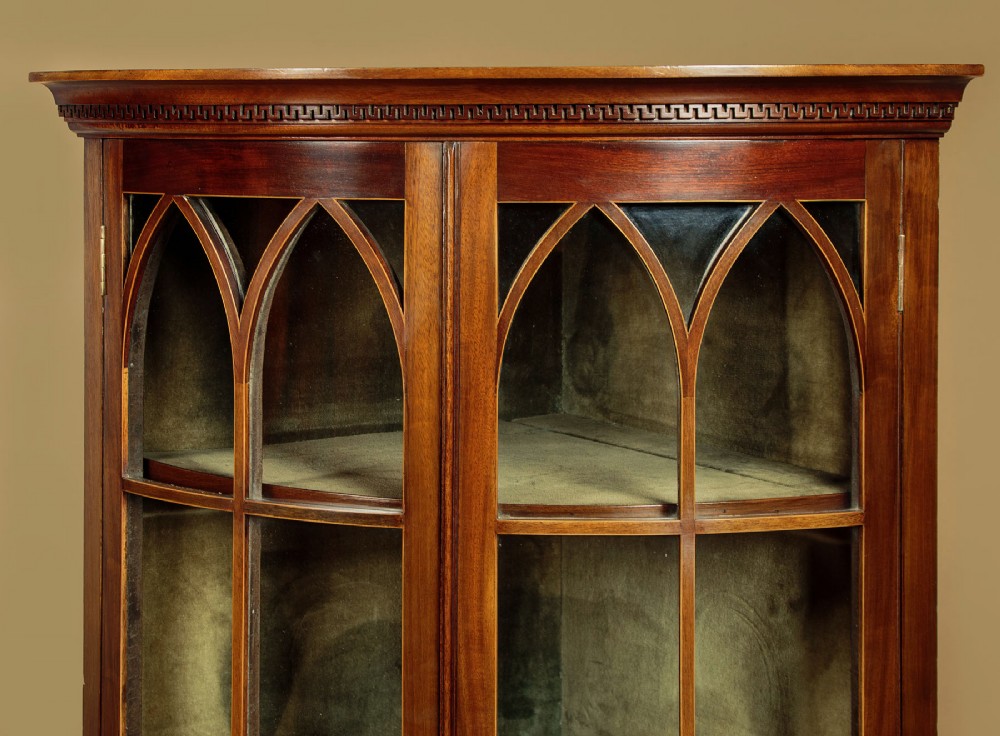 A two-tiered mahogany bow front corner display cabinet featuring upper gothic arch astragal glazing and lower glass panels. View VI