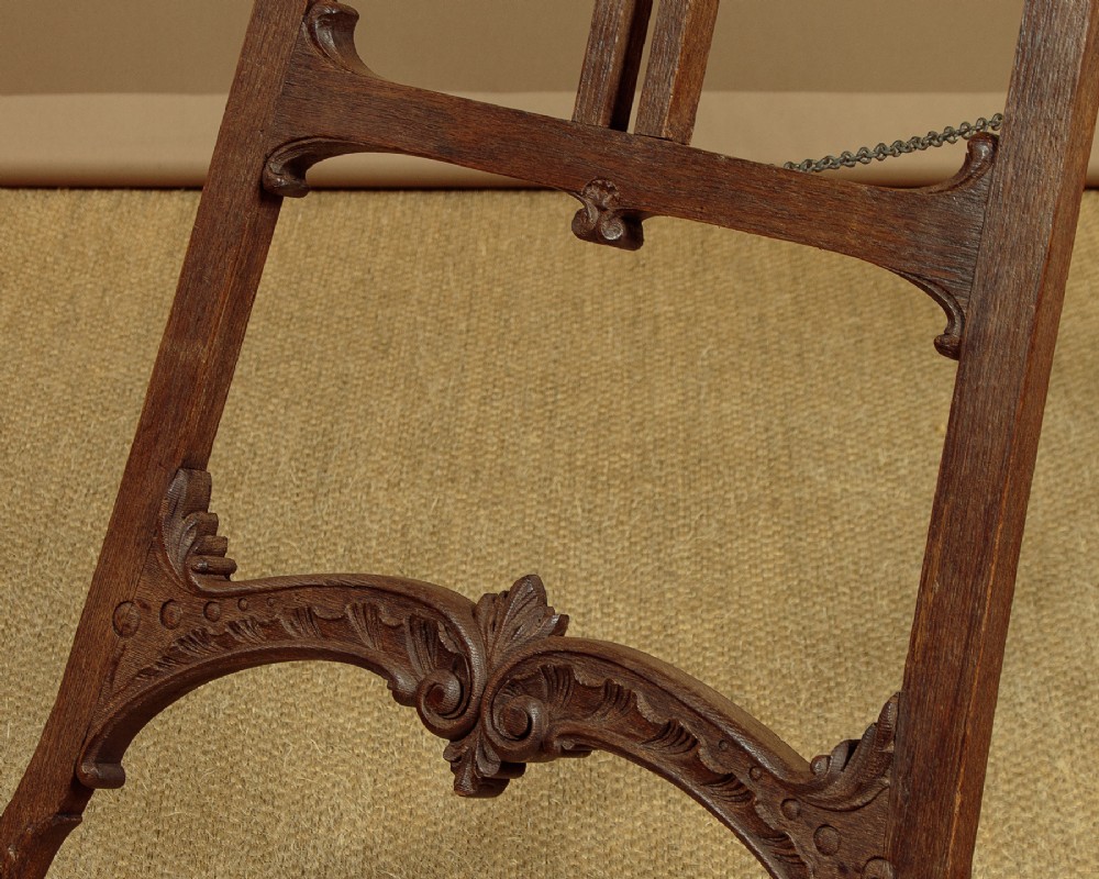 An Edwardian carved oak floor-standing display easel with scroll feet and adjustable wooden support pegs. View VI
