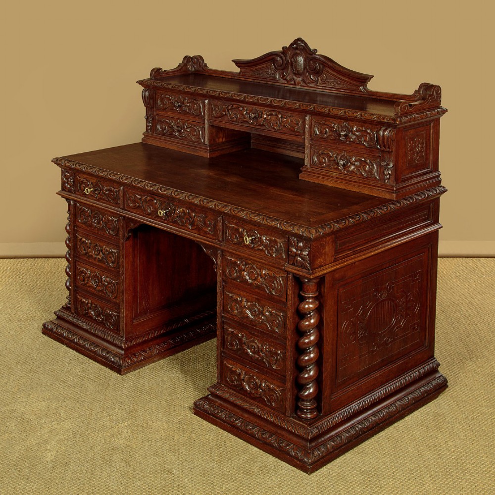 A late 19th-century dark carved oak kneehole desk featuring elaborate scrollwork carving, barley twist corner supports, and a raised superstructure with small drawers.