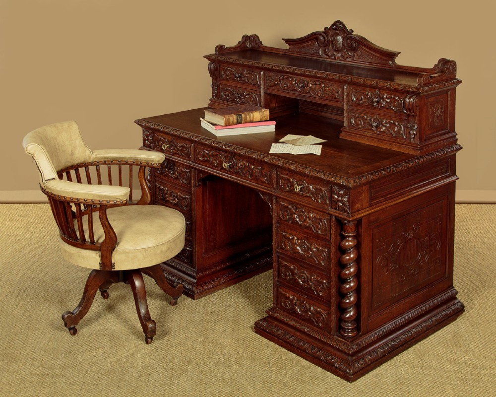 A late 19th-century dark carved oak kneehole desk featuring elaborate scrollwork carving, barley twist corner supports, and a raised superstructure with small drawers. View II