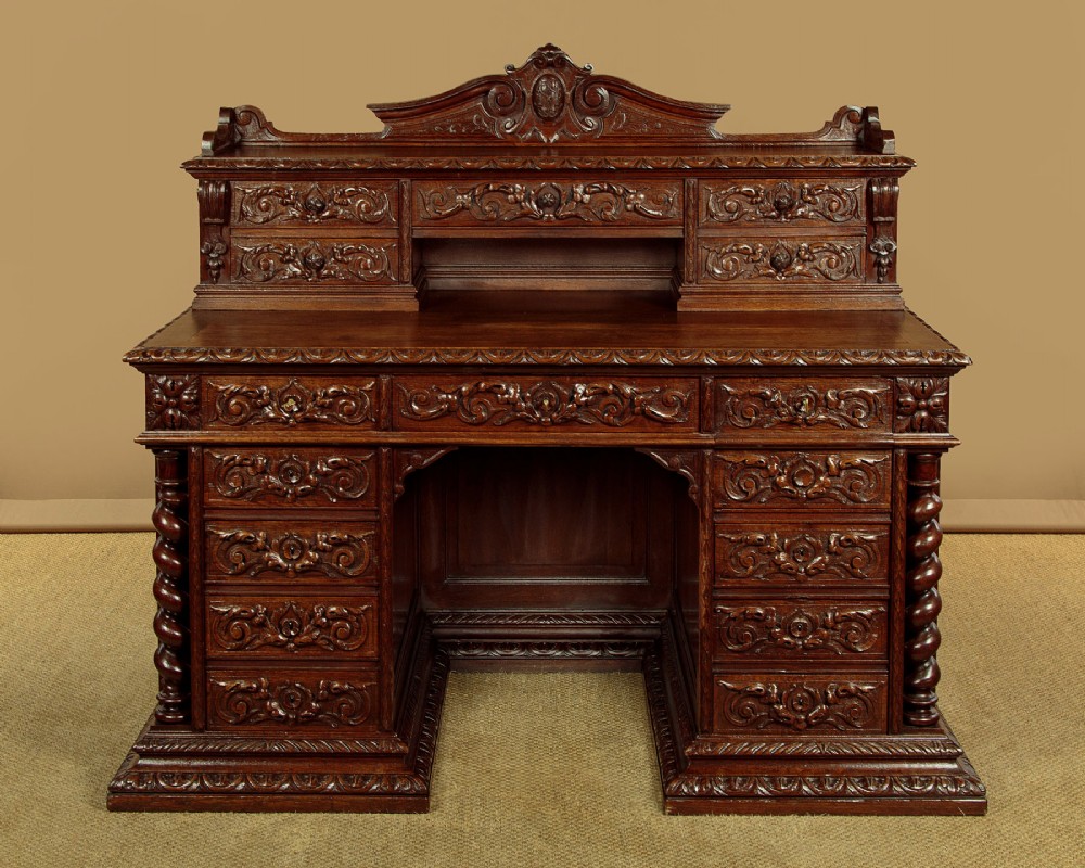 A late 19th-century dark carved oak kneehole desk featuring elaborate scrollwork carving, barley twist corner supports, and a raised superstructure with small drawers. View III