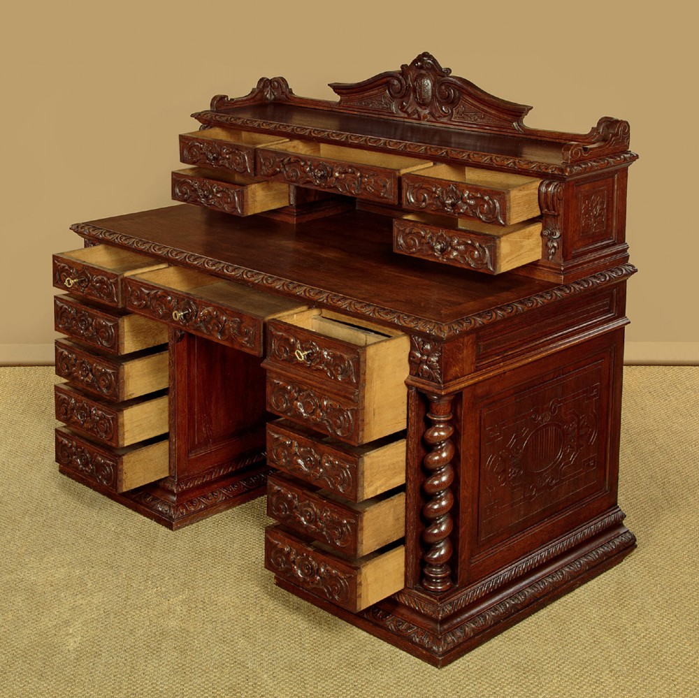 A late 19th-century dark carved oak kneehole desk featuring elaborate scrollwork carving, barley twist corner supports, and a raised superstructure with small drawers. View V