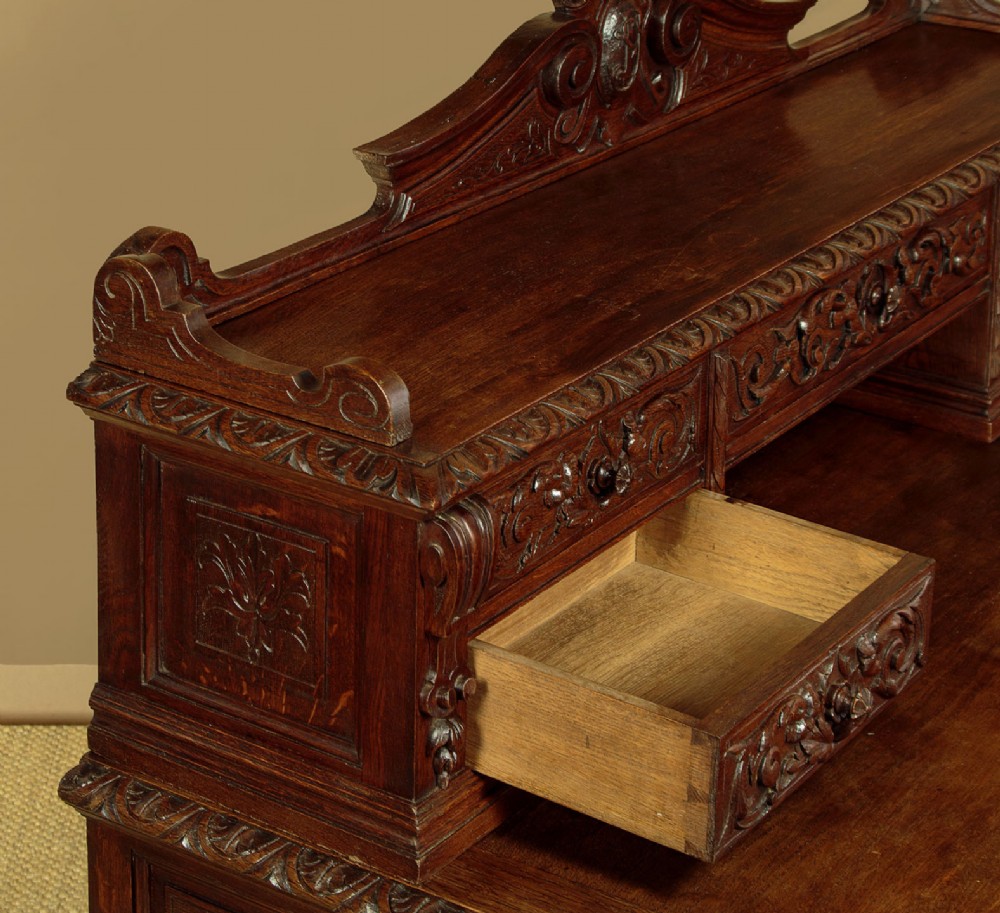A late 19th-century dark carved oak kneehole desk featuring elaborate scrollwork carving, barley twist corner supports, and a raised superstructure with small drawers. View VI