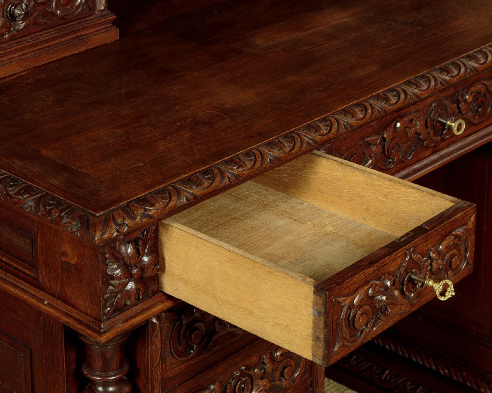 A late 19th-century dark carved oak kneehole desk featuring elaborate scrollwork carving, barley twist corner supports, and a raised superstructure with small drawers. View IX