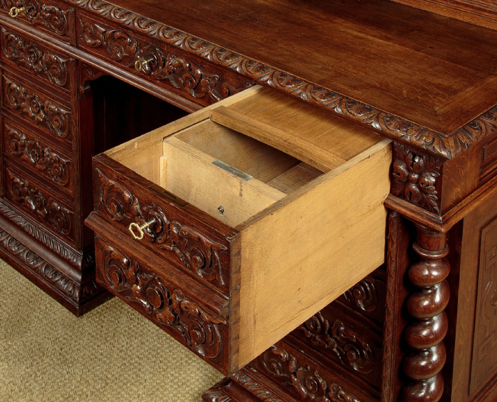 A late 19th-century dark carved oak kneehole desk featuring elaborate scrollwork carving, barley twist corner supports, and a raised superstructure with small drawers. View X