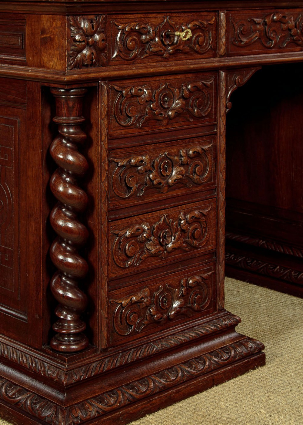A late 19th-century dark carved oak kneehole desk featuring elaborate scrollwork carving, barley twist corner supports, and a raised superstructure with small drawers. View XI