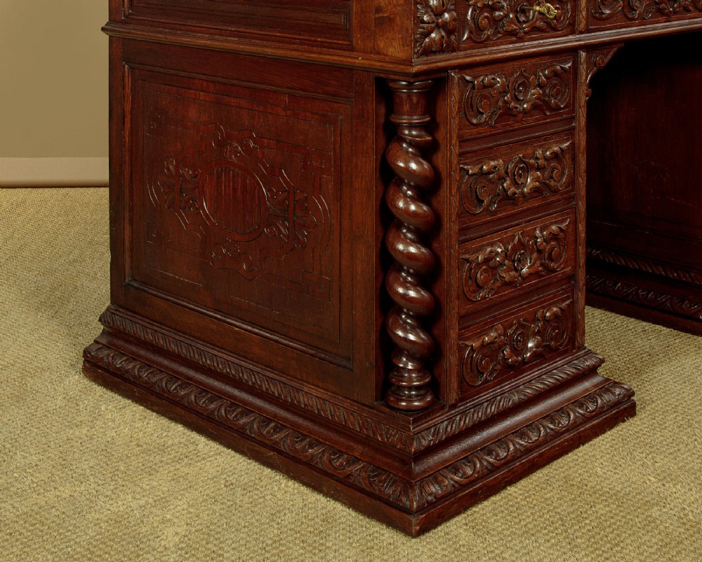 A late 19th-century dark carved oak kneehole desk featuring elaborate scrollwork carving, barley twist corner supports, and a raised superstructure with small drawers. View XII