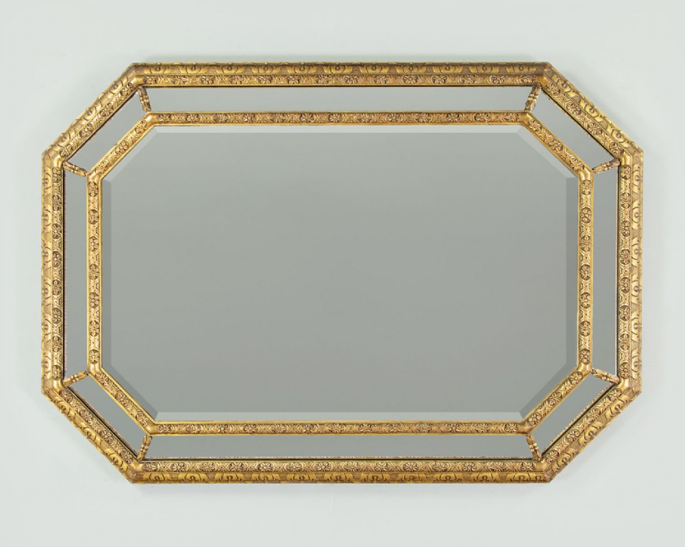 An octagonal gilded cushion frame mirror featuring floral embossed moulding and bevelled mirror inserts around a central glass plate.