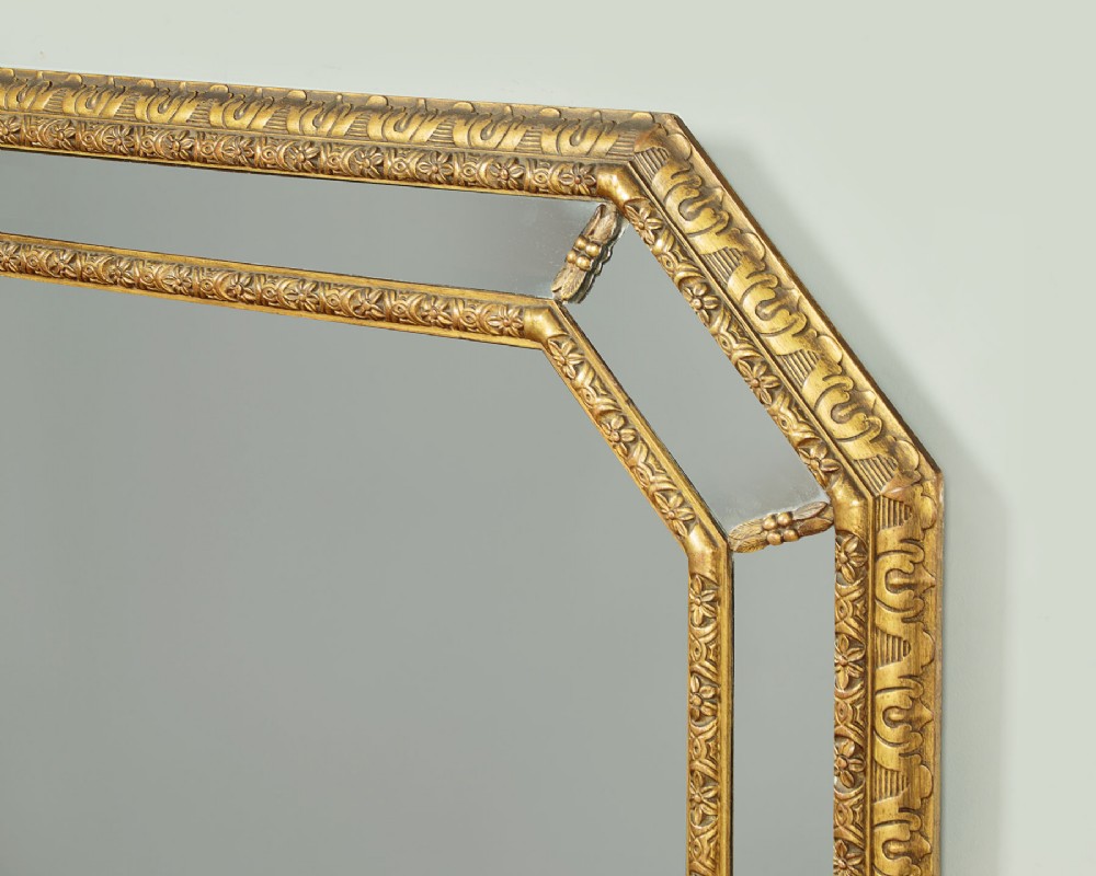 An octagonal gilded cushion frame mirror featuring floral embossed moulding and bevelled mirror inserts around a central glass plate. View V