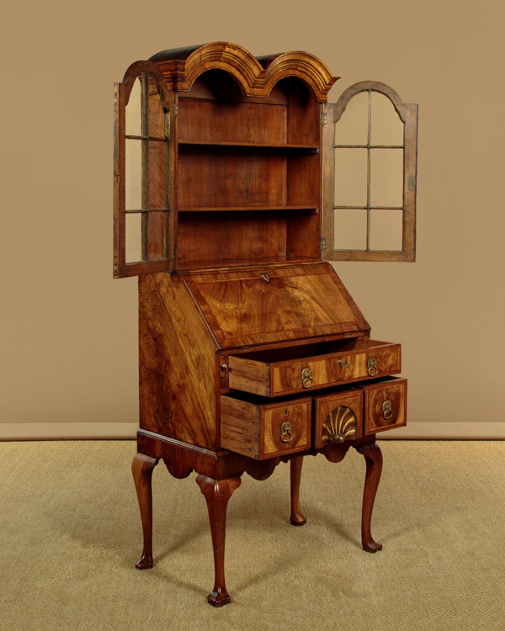 A Queen Anne style walnut bureau bookcase featuring a double-domed top, glazed upper doors, a slant-front writing slope, lower drawers with a carved shell motif, and slender cabriole legs. View V