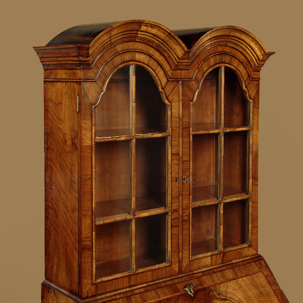 A Queen Anne style walnut bureau bookcase featuring a double-domed top, glazed upper doors, a slant-front writing slope, lower drawers with a carved shell motif, and slender cabriole legs. View VI